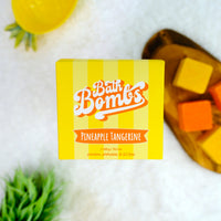 Yellow box of Pineapple Tangerine bath bombs with a wooden board of bath bombs in the background.