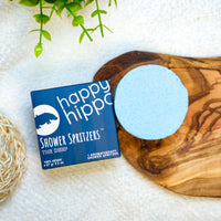 Happy Hippo Shower Spritzer packaging with a blue round product on a wooden board.