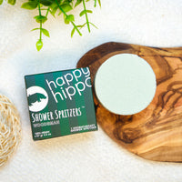 Happy Hippo Shower Spritzers packaging on a wooden board with a plant in the background