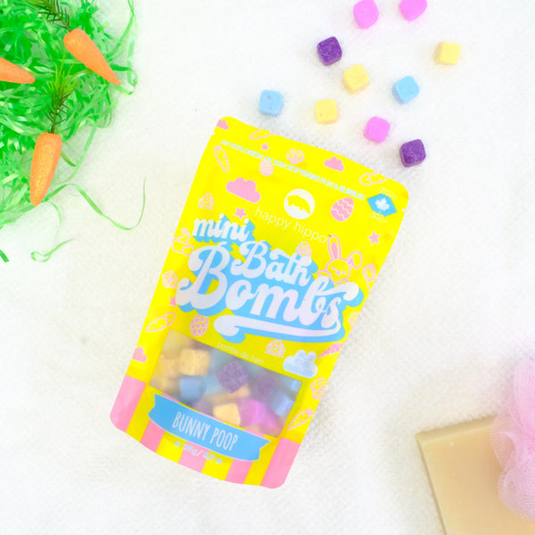 Bag of yellow Bunny Poop Mini Bath Bombs on a white background with mini bath bombs scattered around it