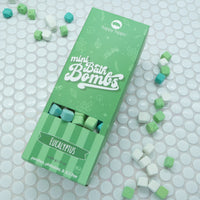 Light green box of Coldbuster Mini Bath Bombs on a white background with bath bombs scattered around it