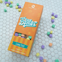 Orange box of Llama Poop Mini Bath Bombs on a white background with bath bombs scattered around it