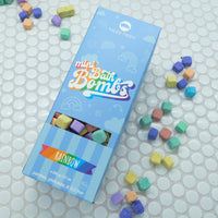 Light blue box of Rainbow Mini Bath Bombs on a white background with bath bombs scattered around it